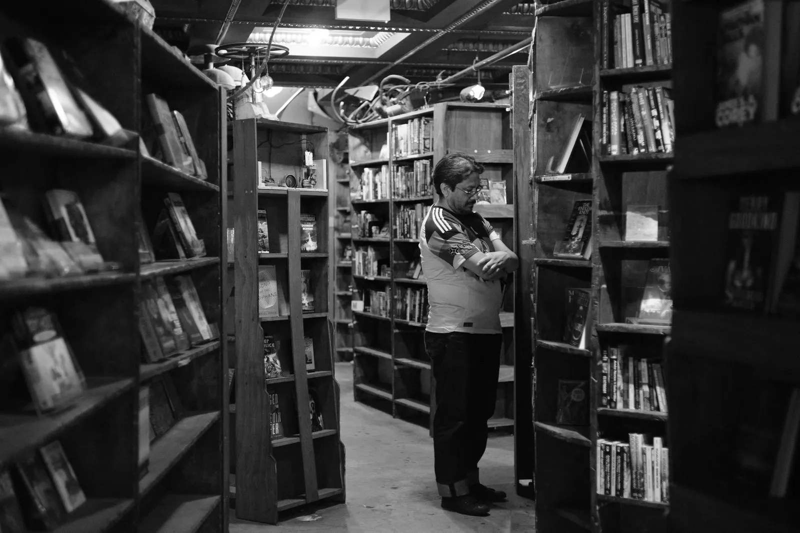 A man browsing books in a cozy, dimly lit library with wooden shelves.